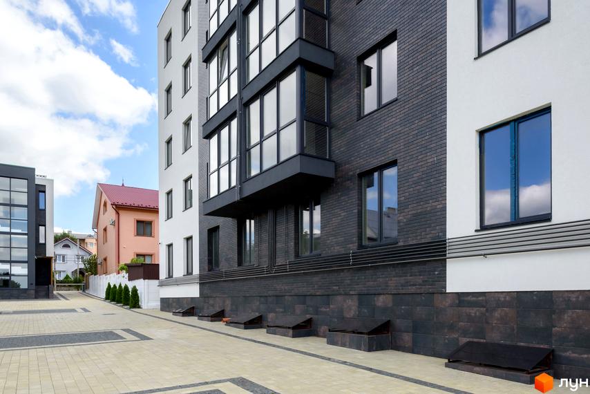 Зовнішній вигляд новобудови ЖК Center з цегляним фасадом та великими вікнами. Прибудинкова територія вимощена плиткою.