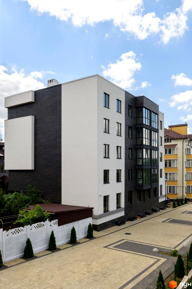 Житловий комплекс Center: фасад будинку з білою та темно-сірою обробкою, панорамне скління, прибудинкова територія з вимощенням та зеленими насадженнями.