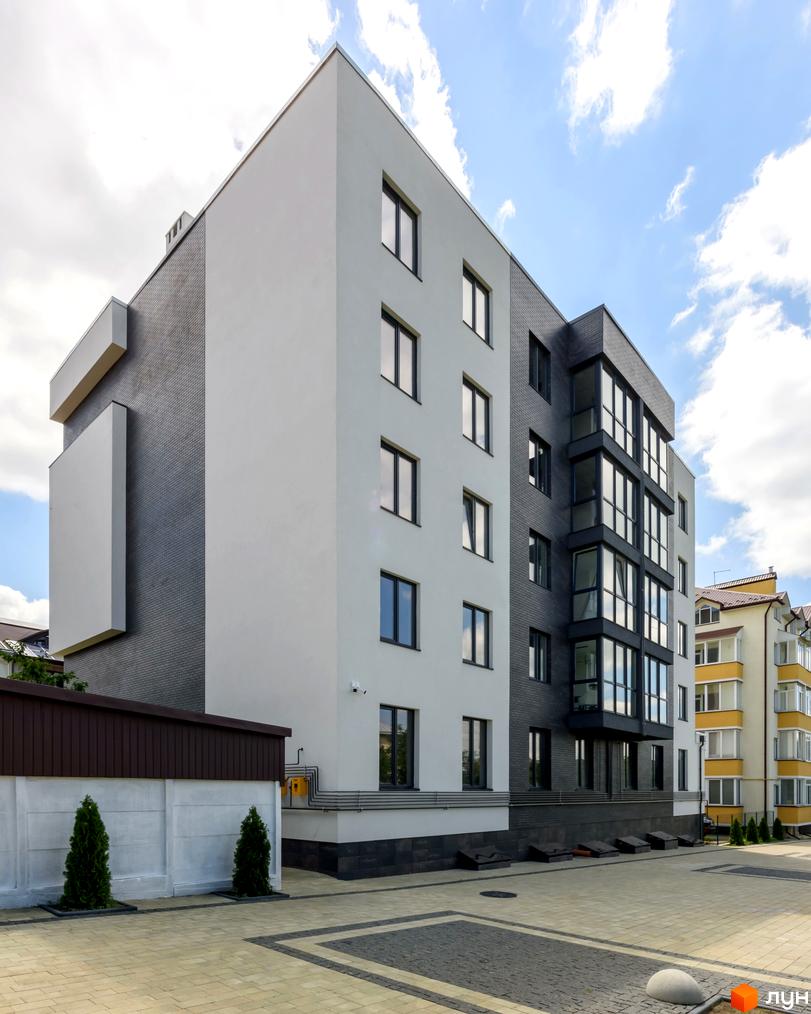 Зовнішній вигляд новобудови ЖК Center з білою та сірою цегляною обробкою, панорамними вікнами та впорядкованою прибудинковою територією з бруківкою та зеленими насадженнями.