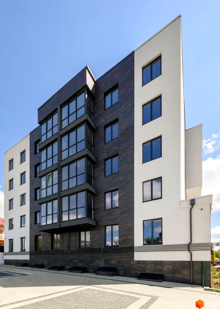 Зовнішній вигляд житлового комплексу Center з білою та темно-сірою цегляною обробкою, великими вікнами та сірим балконом. Прибудинкова територія викладена бруківкою.