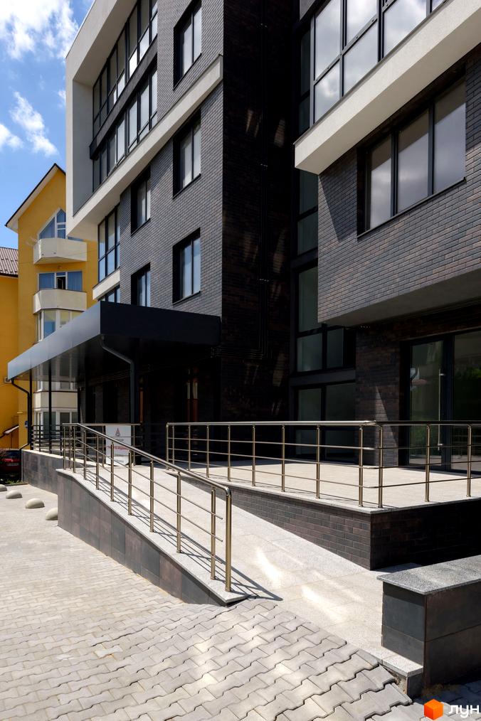 Зовнішній вигляд новобудови ЖК Center з цегляним фасадом та пандусом для доступності. Прибудинкова територія з бруківкою та огорожею.