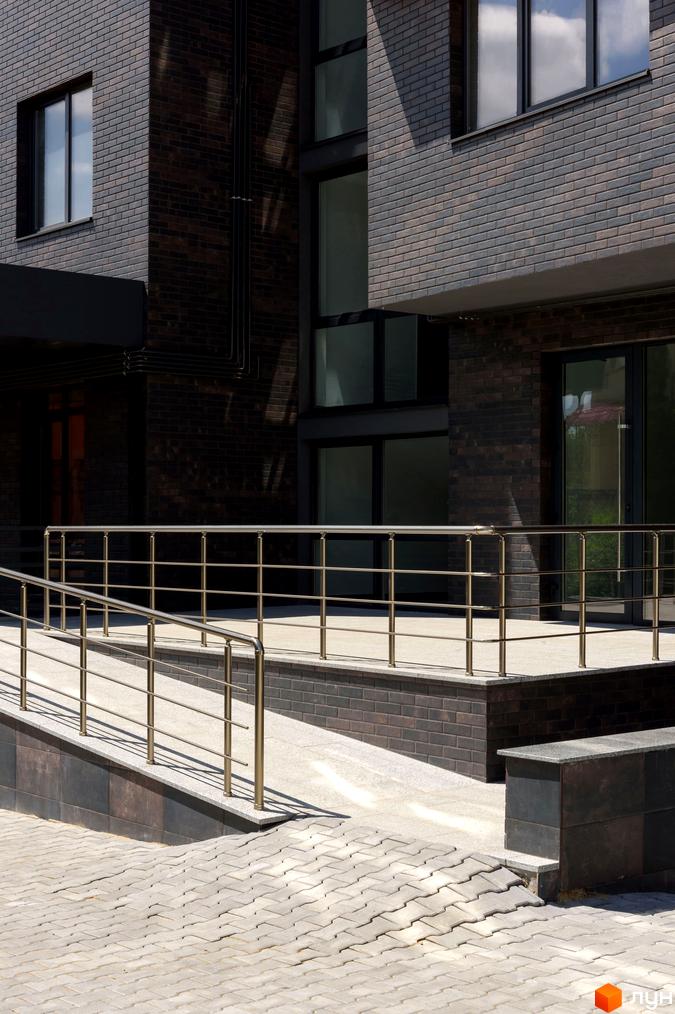 Зовнішній вигляд будинку ЖК Center з цегляним фасадом та пандусом з поручнями. Прибудинкова територія вимощена плиткою.