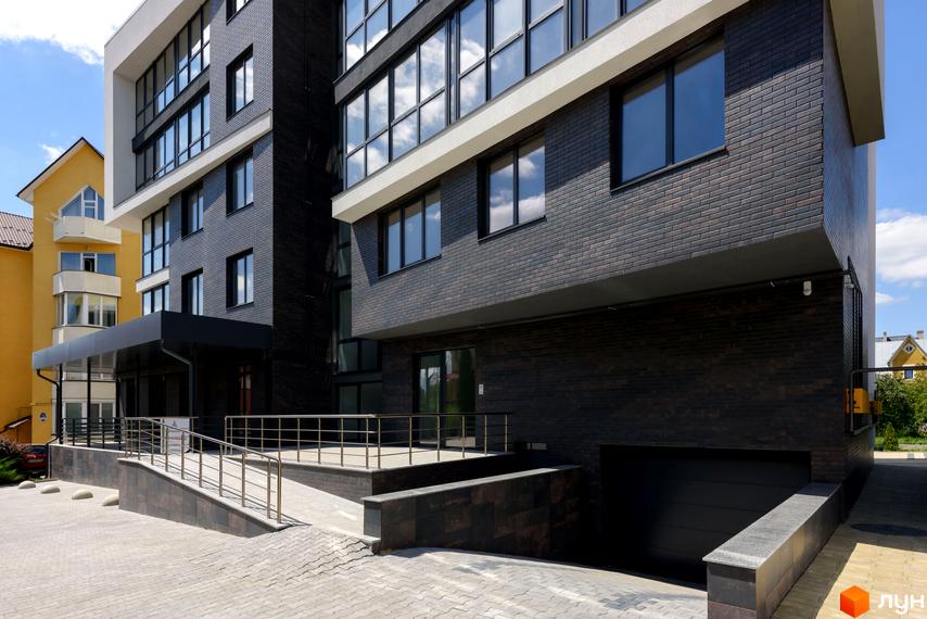 Фасад житлового комплексу Center з темної цегли та білих елементів, з пандусом та прибудинковою територією.