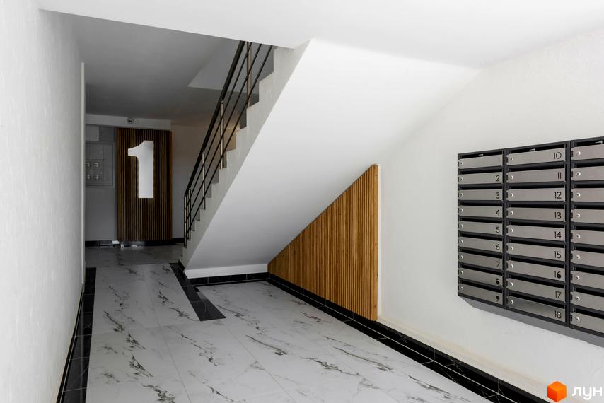 Інтер'єр під'їзду в Будівельному проєкті KromaxBud з поштовими скриньками та сходовим майданчиком. Мармурова плитка на підлозі, дерев'яні панелі на стінах.
