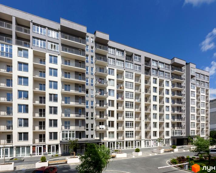 Фото новобудови ЖК KromaxBud з балконами та великою кількістю вікон. На прибудинковій території розташовані лавки та зелені насадження.