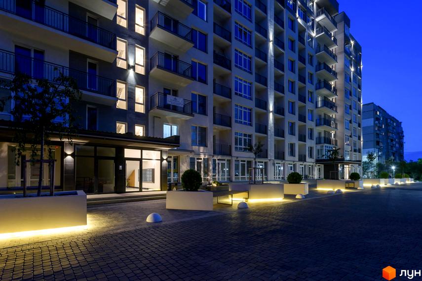 Фото фасаду багатоповерхового будинку ЖК KromaxBud з балконами та великими вікнами. На передньому плані прибудинкова територія з тротуарною плиткою.