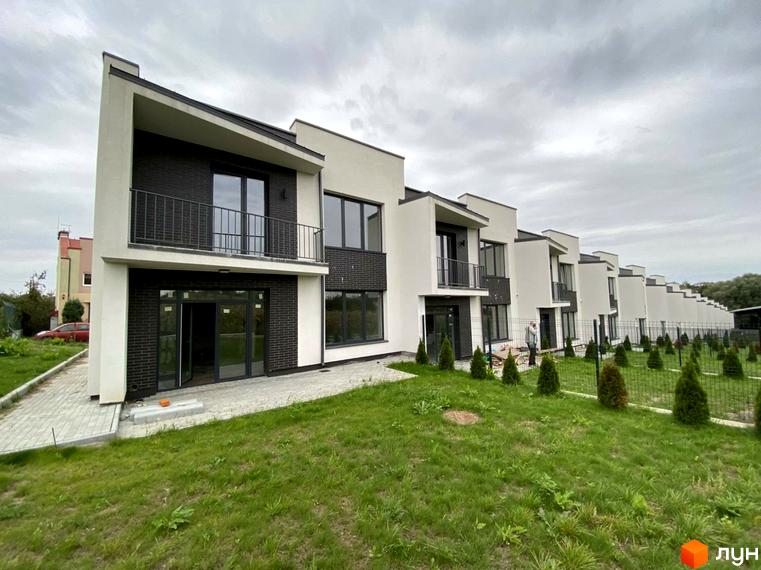 Таунхауси Rubicon Cottages з білим та чорним фасадом, балконами та великими вікнами, розташовані на зеленій ділянці з молодими деревами.