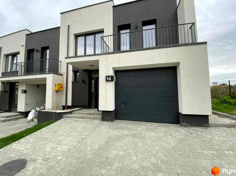 Зовнішній вигляд таунхаусів Rubicon Cottages з сірими гаражними воротами та бруківкою перед будинками. Сучасна архітектура з білими та темними фасадами.