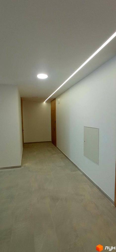 Коридор новобудови ЖК Rubicon Premium з підсвічуванням стелі та дверима. Підлогове покриття сірого кольору.