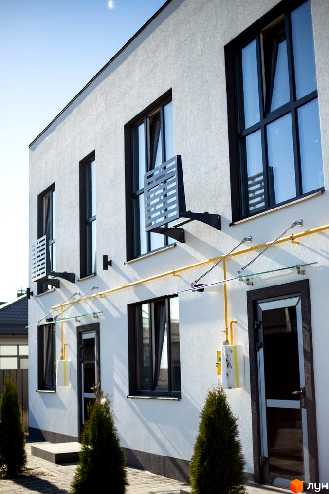 Фасад будинку житлового комплексу DREAM HOUSE з великими вікнами та газовим стояком. Навколо будинку висаджені туї та вимощена бруківка.