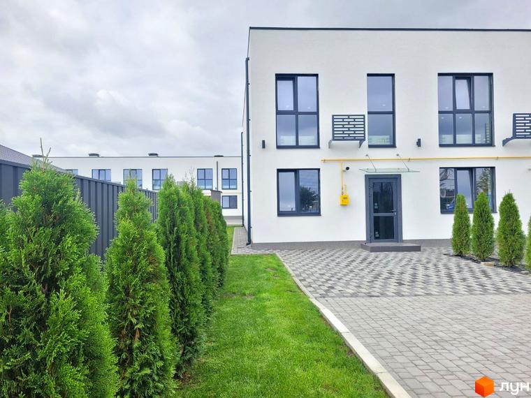 Білі двоповерхові таунхауси DREAM HOUSE з темними вікнами та вхідними дверима, бруківка та зелені насадження біля будинку.