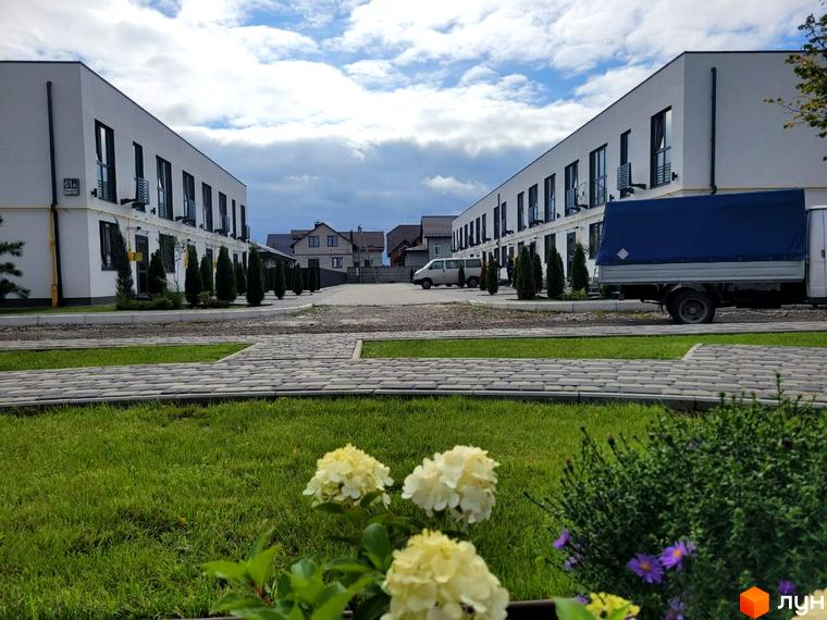 Таунхауси DREAM HOUSE - двоповерхові будинки з білими фасадами та чорними вікнами, розташовані на доглянутій території з газоном та бруківкою.