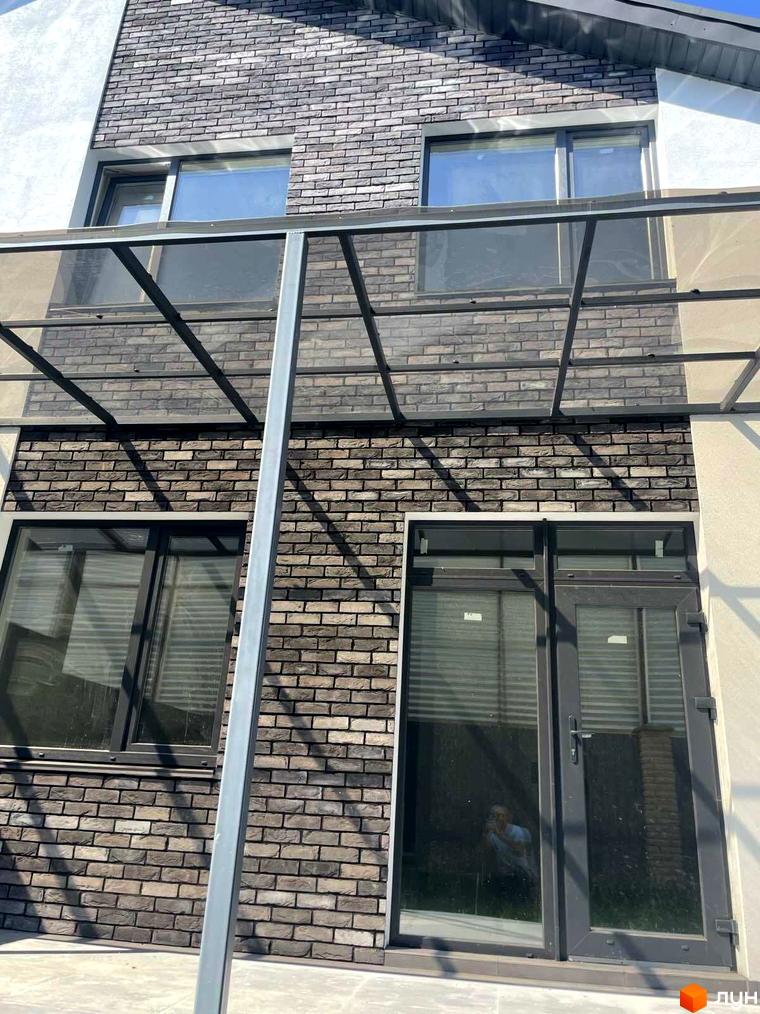 Фасад будинку з цегляним оздобленням та великими вікнами житлового комплексу Дуплекси „На Драгоманова“. Зовнішній вигляд новобудови з навісом.