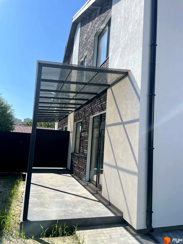 Зовнішній вигляд будинку з навісом та цегляним фасадом, прибудинкова територія з плиткою та зеленню. Дуплекси „На Драгоманова“ – ваш новий дім.