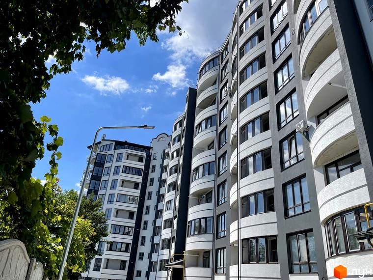 Житловий комплекс Трускавецька Фортеця: високі будинки з округлими балконами та темними вікнами. Видно зелень дерев та ліхтар.