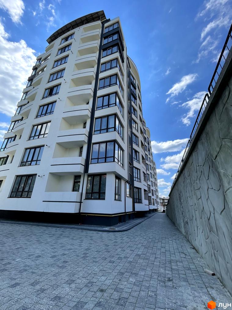 Зображення фасаду та прибудинкової території Житлового комплексу Трускавецька Фортеця. Багатоповерховий будинок з великими вікнами та балконами.