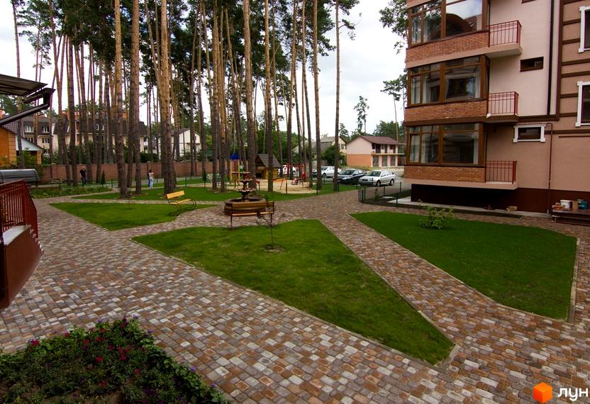 Житловий комплекс Жемчужина города з цегляним фасадом та балконами. На прибудинковій території розташовані доріжки з бруківки, зелена галявина та дитячий майданчик.