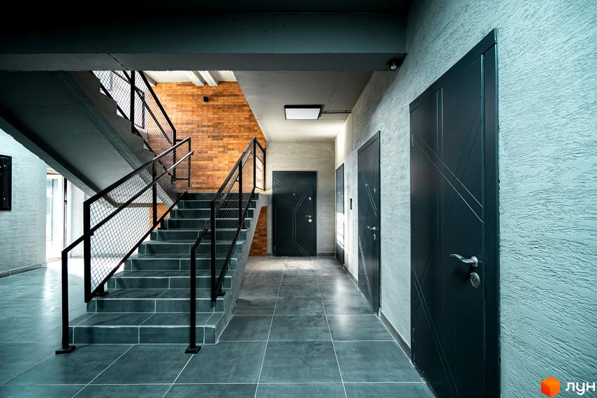 Комплекс Клубне містечко 12: сходова клітка з цегляною стіною та дверима. Зовнішній вигляд новобудови.