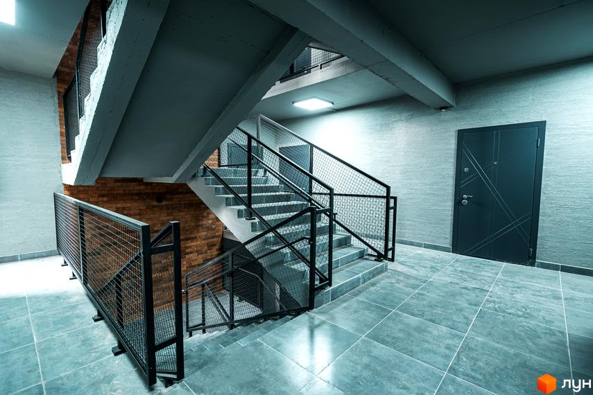 Клубне містечко 12: сучасний під'їзд з бетонними сходами та металевими перилами, цегляною стіною та сірими плитками на підлозі.
