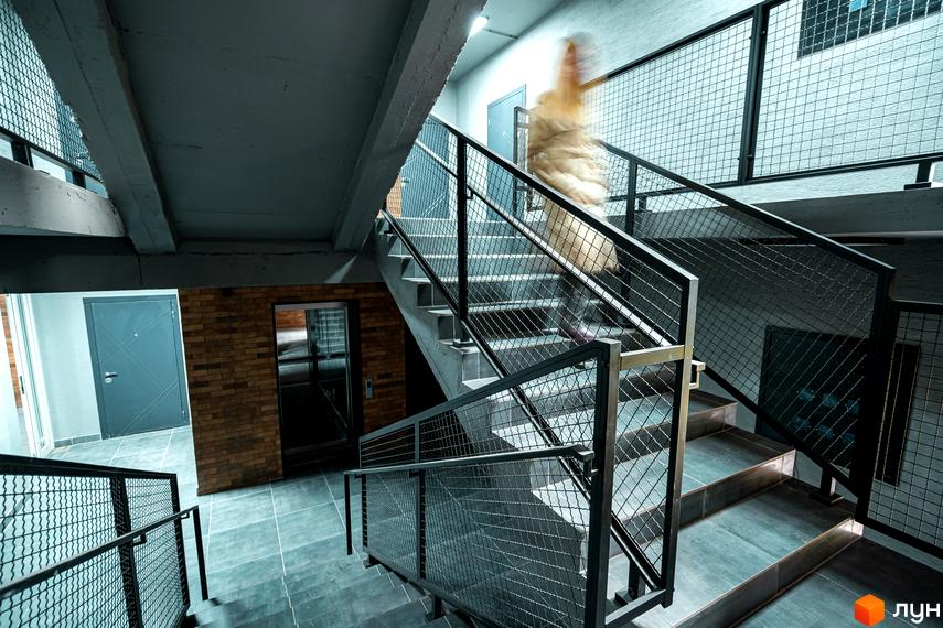 Сучасний житловий комплекс Клубне містечко 12 з бетонними сходовими маршами та сітчастими огорожами. Вхідна група з дверима та ліфтом.