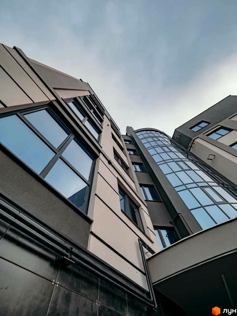 Висотна будівля житлового комплексу з панорамними вікнами на вулиці Коперника, 83. Фасад будинку виконаний у світлих тонах з темними акцентами.