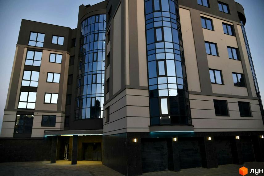 Фасад житлового комплексу на вул. Коперника, 83, з великими панорамними вікнами та сірими елементами. Перед будинком розташована прибудинкова територія з освітленням.