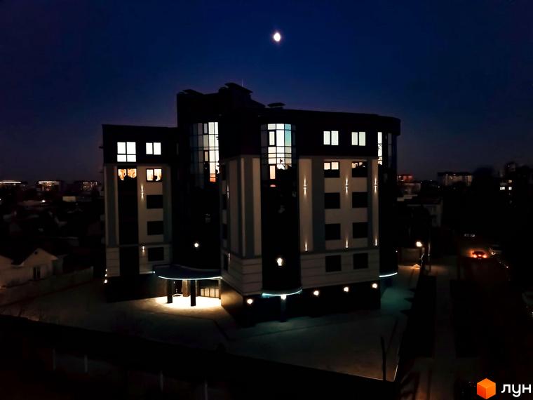 Нічний вигляд житлового комплексу на вул. Коперника, 83, з освітленими вікнами та підсвіченим входом. Навколо будівлі видно прибудинкову територію та сусідні будинки.