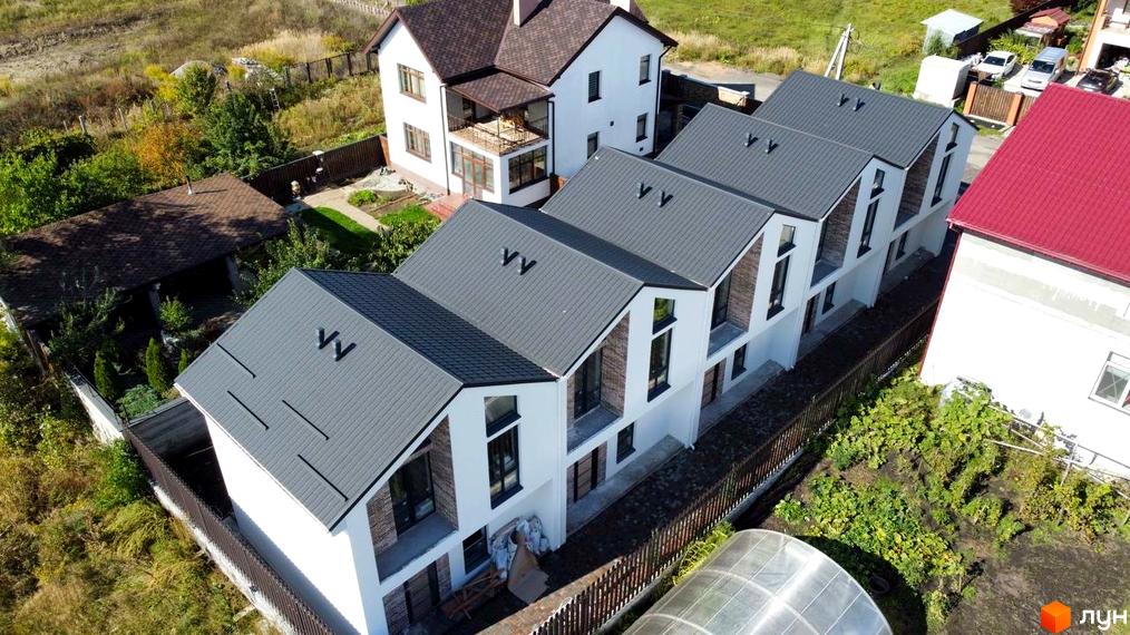 Таунхауси West Homes - сучасний будівельний проєкт з білими фасадами та сірими дахами. На прибудинковій території розташовані зелені насадження та паркан.