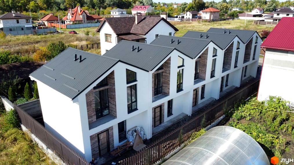 Таунхауси West Homes з сірими дахами та білими фасадами, розташовані на фоні зелених дерев та інших будинків. Біля будинків видно паркан та ділянку з рослинністю.