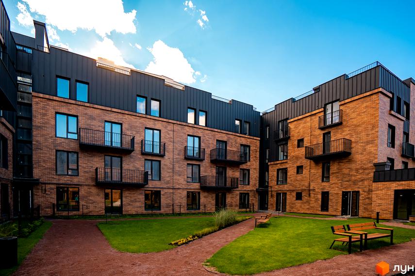 Житловий комплекс Клубне містечко 12 з цегляними фасадами та чорними дахами, внутрішній двір з газоном та лавками.