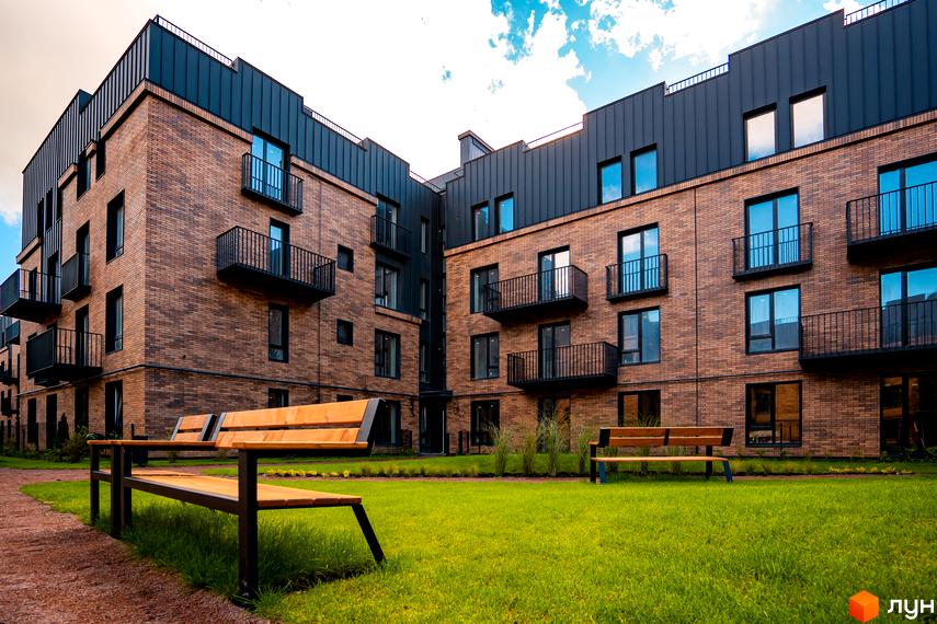 Сучасний житловий комплекс Клубне містечко 12 з цегляним фасадом та балконами. На прибудинковій території зелений газон та лавки.