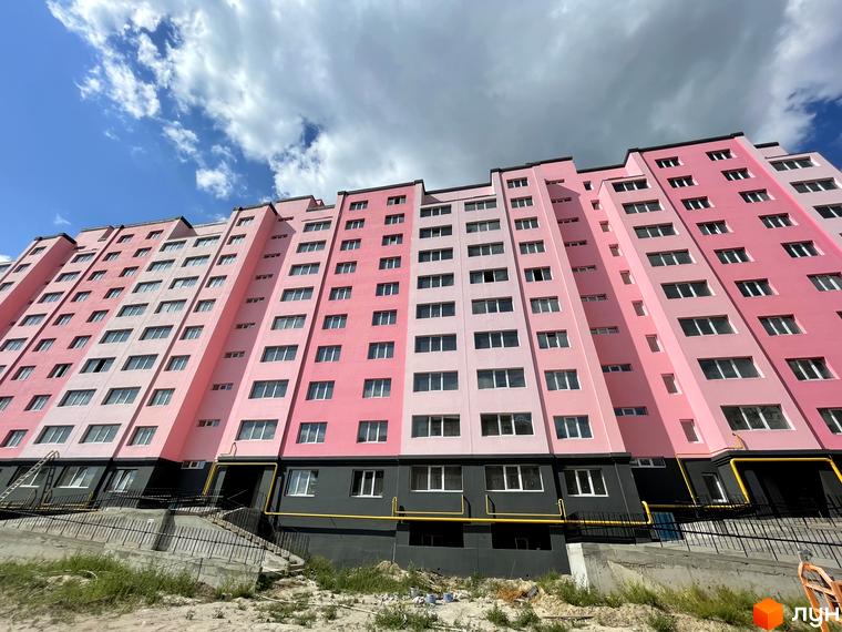 Фасад житлового комплексу Світанок, виконаний у рожевих та світло-рожевих тонах, з сірою нижньою частиною. Навколо новобудови облаштовується прибудинкова територія.