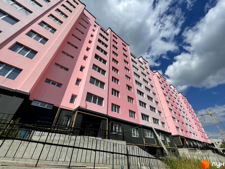 Зовнішній вигляд рожевої новобудови ЖК Світанок з численними вікнами. На передньому плані видно бетонний фундамент та чорну огорожу.