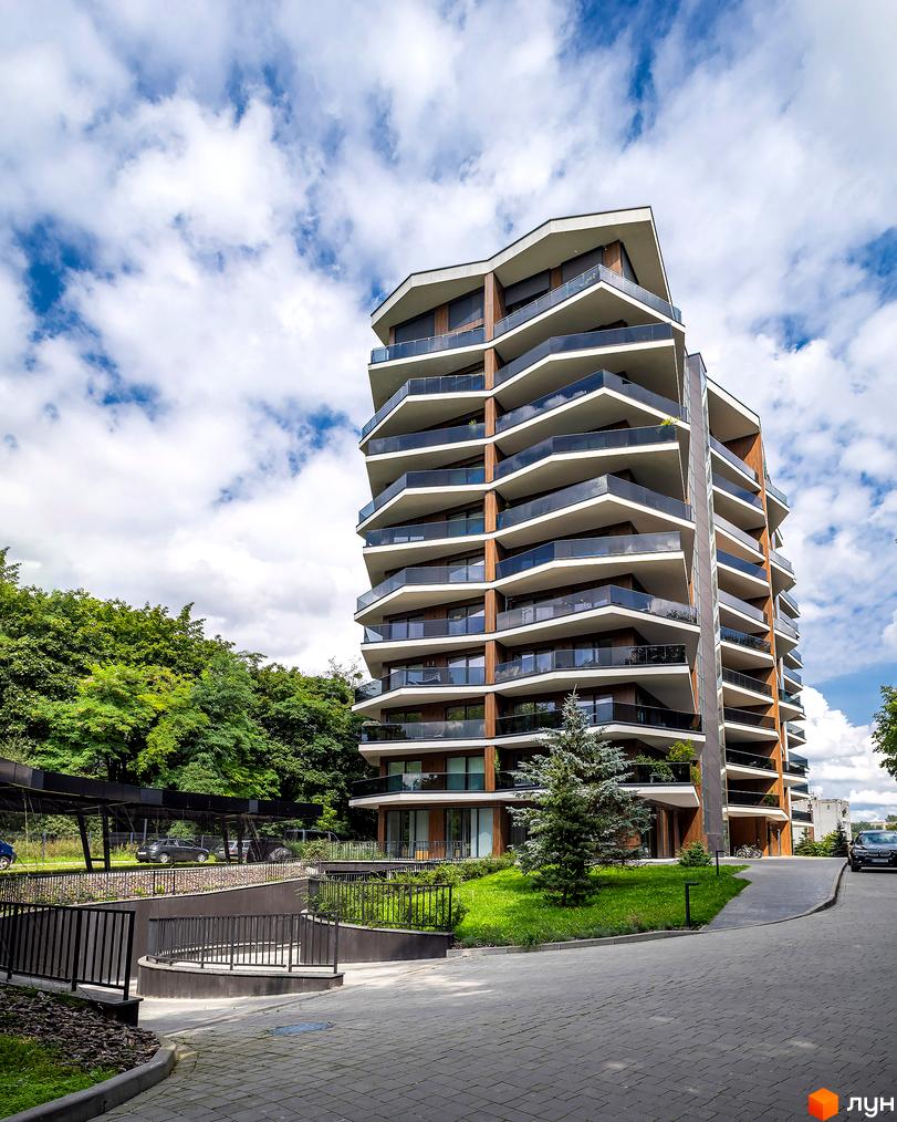 Житловий комплекс Avalon Lux з багатошаровими балконами та скляними перилами на тлі хмарного неба. Прибудинкова територія з доглянутим газоном та деревами.