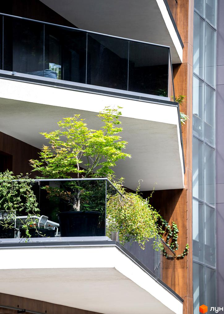 Житловий комплекс Avalon Lux з балконами, озелененням та скляними фасадами. На балконі розташовані дерева та рослини.