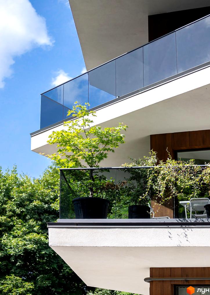 Житловий комплекс Avalon Lux з скляними балконами та зеленими насадженнями. Зовнішній вигляд будинку з сучасними елементами та зеленню на балконах.