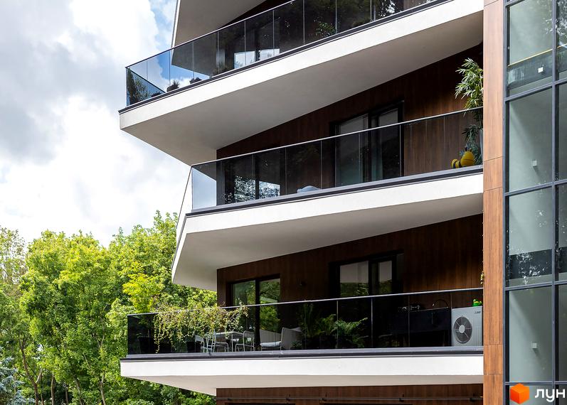 Житловий комплекс Avalon Lux з сучасними балконами та скляними перилами. Навколо зелені дерева та блакитне небо.