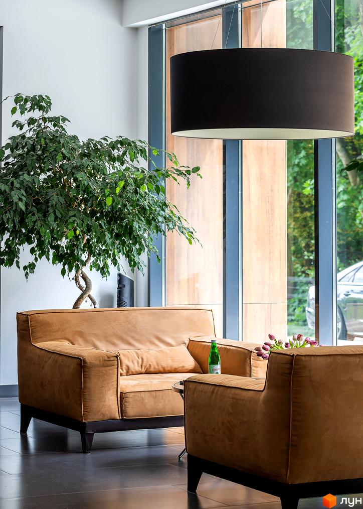 Інтер'єр ЖК Avalon Lux з коричневими диванами та великою рослиною біля вікна. Сучасний дизайн простору для відпочинку.
