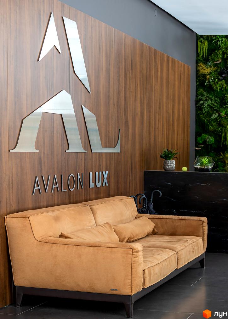 Інтер'єр лобі житлового комплексу Avalon Lux з диваном та логотипом на стіні. Опис новобудови для просування сайту.