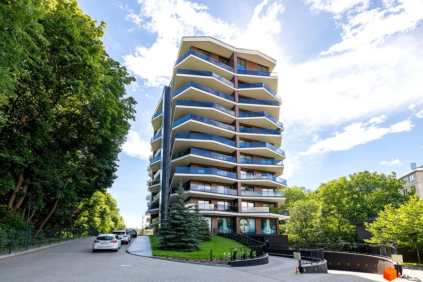 Новобудова Avalon Lux з балконами та скляними перилами. Територія навколо будинку з деревами та дорогою з автомобілями.