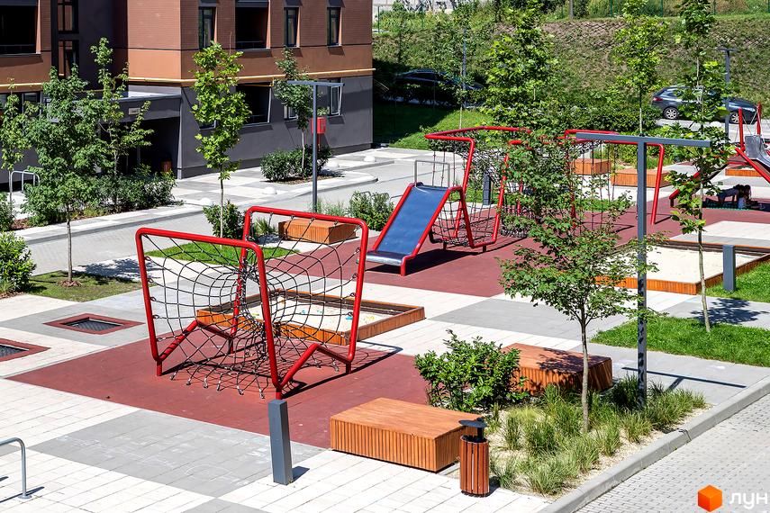 Зображення ігрового майданчика біля будинку Avalon Zelena Street. На фото дитячий майданчик з гіркою, пісочницею та лазанкою.