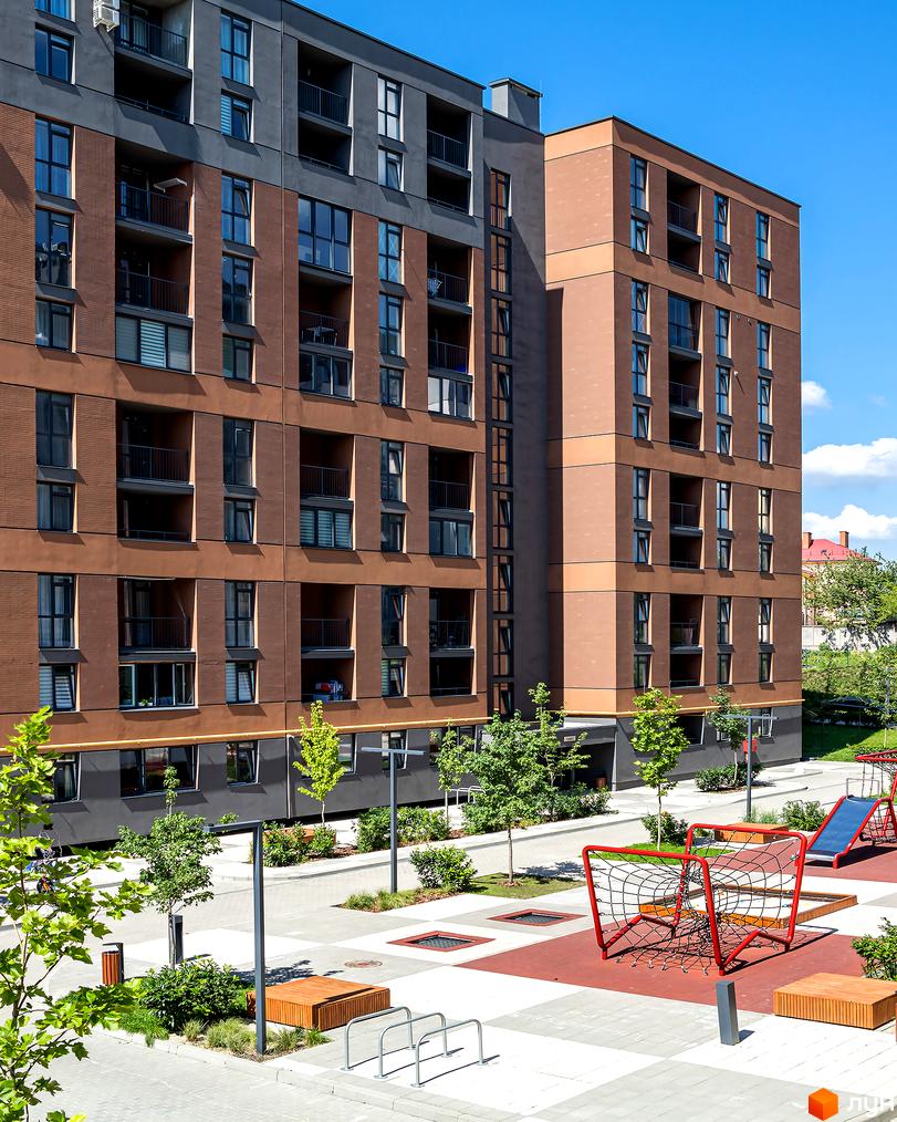 Зовнішній вигляд Житлового комплексу Avalon Zelena Street з фасадом з коричневої цегли та великими вікнами. На передньому плані дитячий майданчик з гіркою та гойдалками.