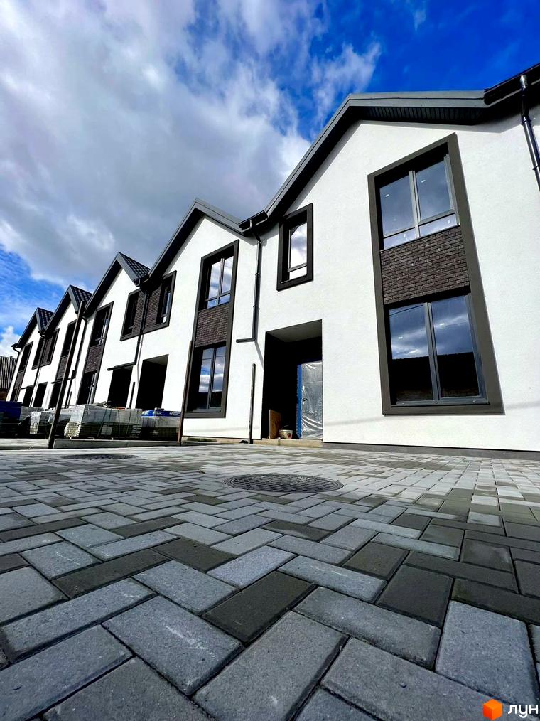 Таунхаус LA-42 з білою штукатуркою, темними вікнами та сірою бруківкою на прибудинковій території. Зовнішній вигляд новобудови.