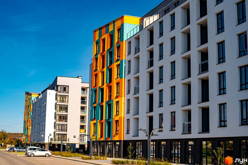 Житловий комплекс Квартал Краківський. Фасади будинків оздоблені яскравими кольорами: жовтим, помаранчевим та бірюзовим. Поруч розташована дорога з припаркованими автомобілями.