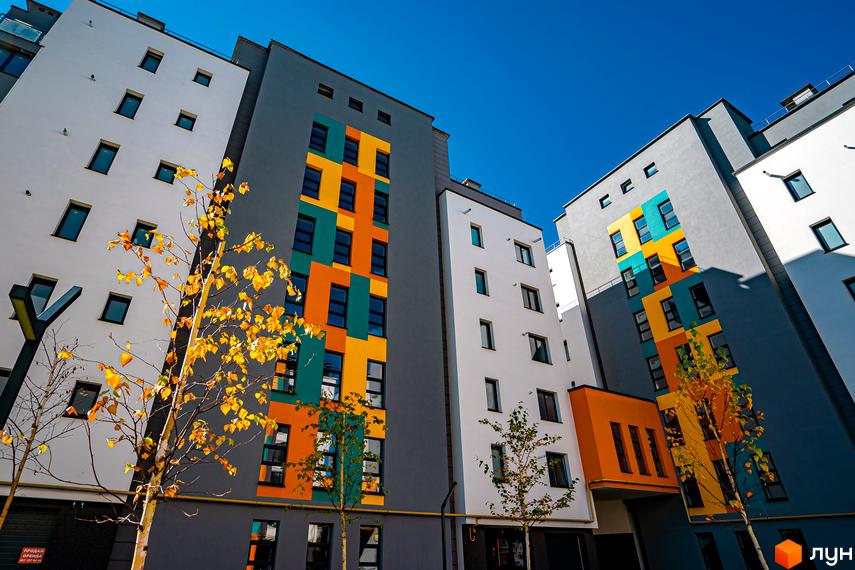 Житловий комплекс Квартал Краківський. Фасади будинків оздоблені яскравими геометричними візерунками в жовтому, бірюзовому та помаранчевому кольорах. Навколо новобудов висаджені дерева з осіннім листям.