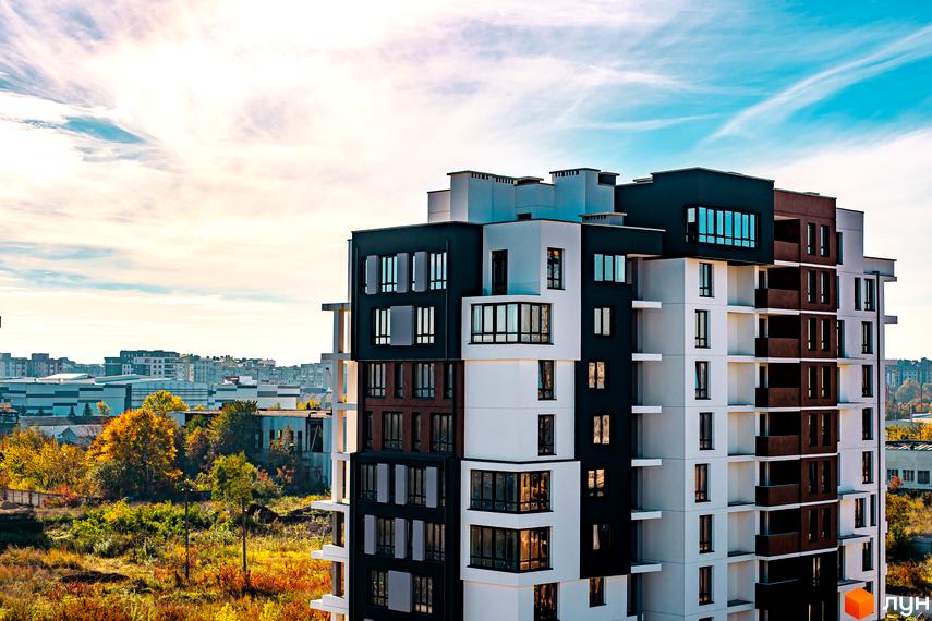 Житловий комплекс Квартал Краківський. Сучасна архітектура новобудови з багатою зеленою територією навколо. На фасаді будинку присутні елементи коричневого, білого та чорного кольорів.