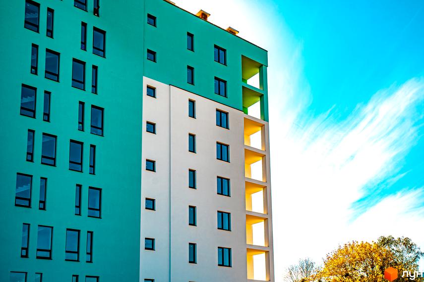 Житловий комплекс Квартал Краківський з біло-бірюзовим фасадом та жовтими балконами на тлі блакитного неба. Фото новобудови.