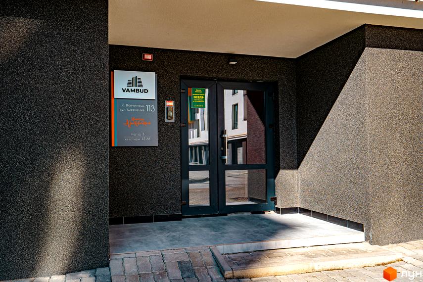 Вхідна група житлового комплексу Квартал Краківський з адресою с. Вовчинець, вул. Шевченка, 113. Зовнішнє оздоблення фасаду темного кольору з фактурною поверхнею.