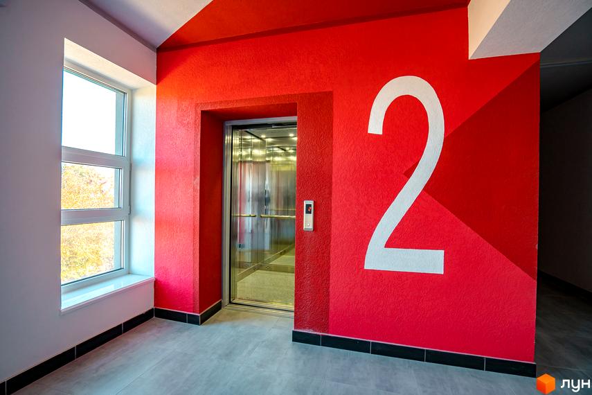 Житловий комплекс Квартал Краківський. Сучасний дизайн холу з ліфтом та великою цифрою 2 на червоній стіні, вікно з видом на дерева.