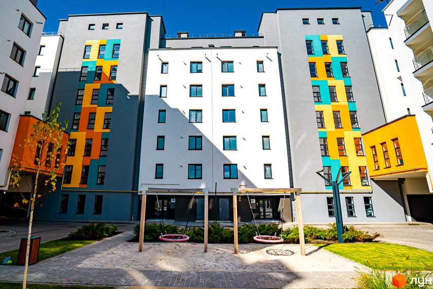 Житловий комплекс Квартал Краківський з яскравим фасадом у бірюзових та жовтих кольорах. Дитячий майданчик з гойдалками на піщаному покритті.